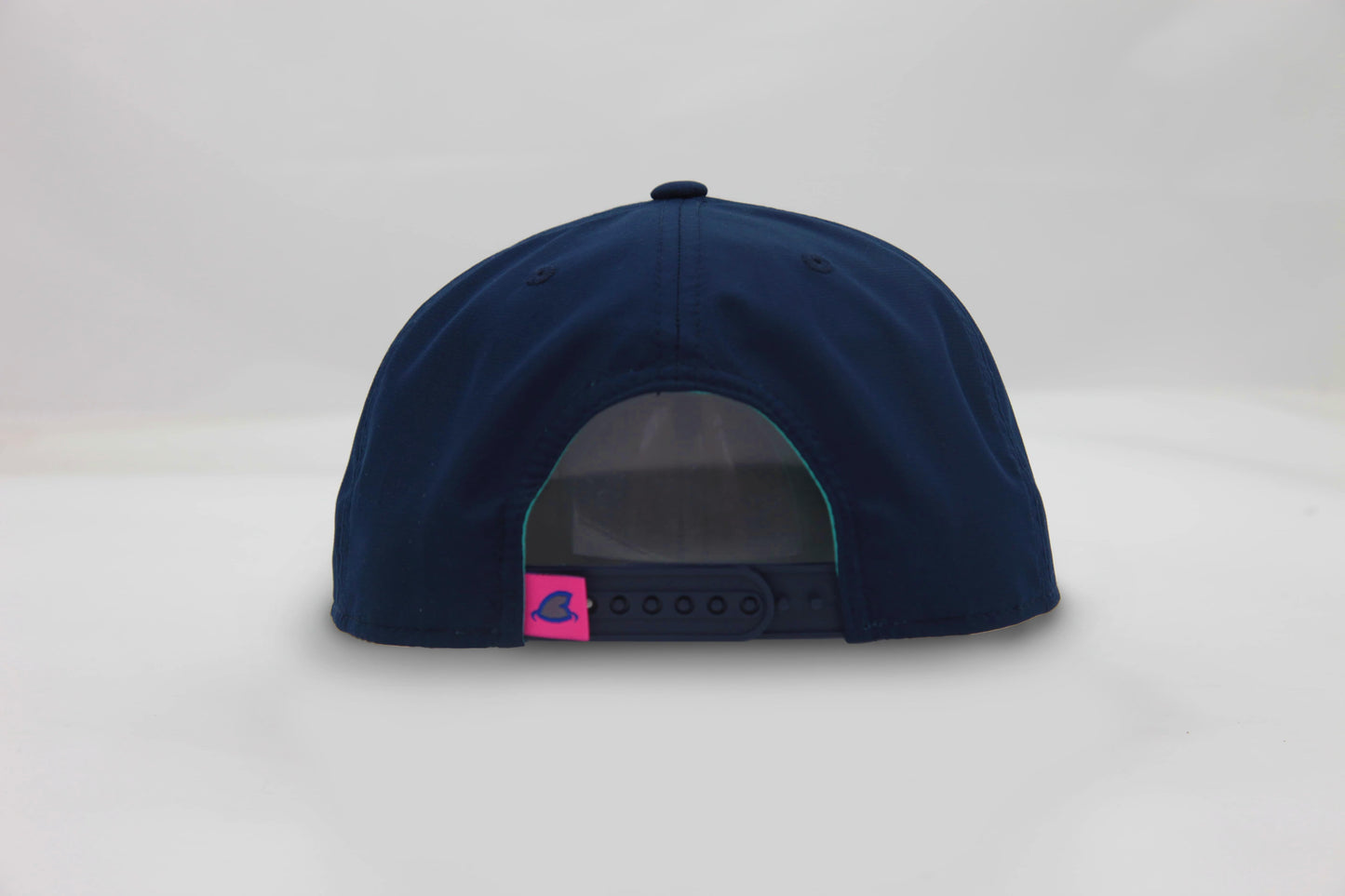 Back view of The Midnight Cruiser ’93 Hat – navy blue cap with snapback closure and small pink loop tag featuring the Maxwell Sharkey fin icon.
