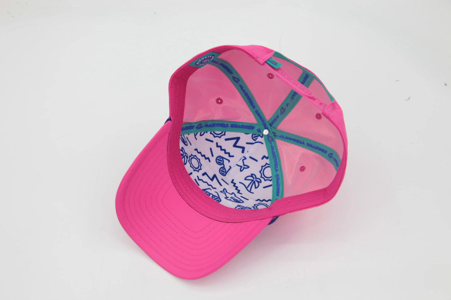 Underbrim view of The Sunset Slasher ’93 Hat – neon printed interior with the Maxwell Sharkey signature Memphis-style patters featuring sun, palm tree, and wave icons. There is teal Maxwell Sharkey logo taping.