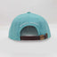 Back view of The Sharkey Cruiser Hat – aqua / teal-colored cap with adjustable brown strap and bronze-colored metal adjuster. Maxwell Sharkey is written in small print across the back of the hat.