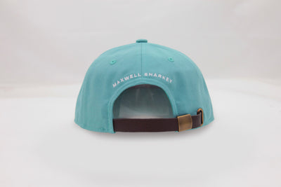 Back view of The Sharkey Cruiser Hat – aqua / teal-colored cap with adjustable brown strap and bronze-colored metal adjuster. Maxwell Sharkey is written in small print across the back of the hat.