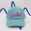 Front view of The Sharkey Cruiser Hat – a teal hat with bold Sharkey script in pink with a white shark fin and water icon behind. 