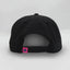 Back view of The Neon Lights Hat – black cap with a pink embroidered loop tag featuring the Maxwell Sharkey fin icon with an adjustable snapback closure.